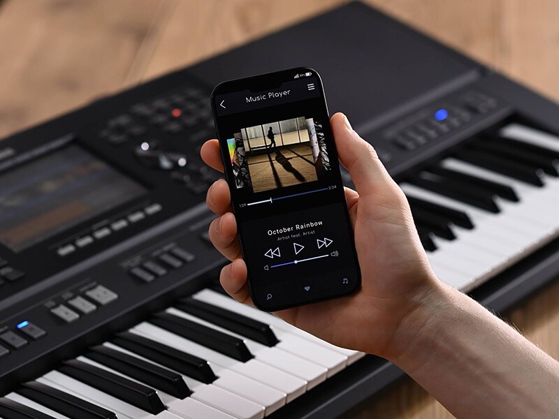 Yamaha Workstation Arranger PSR-SX920 e una mano che tiene uno smartphone con lo schermo di un lettore musicale