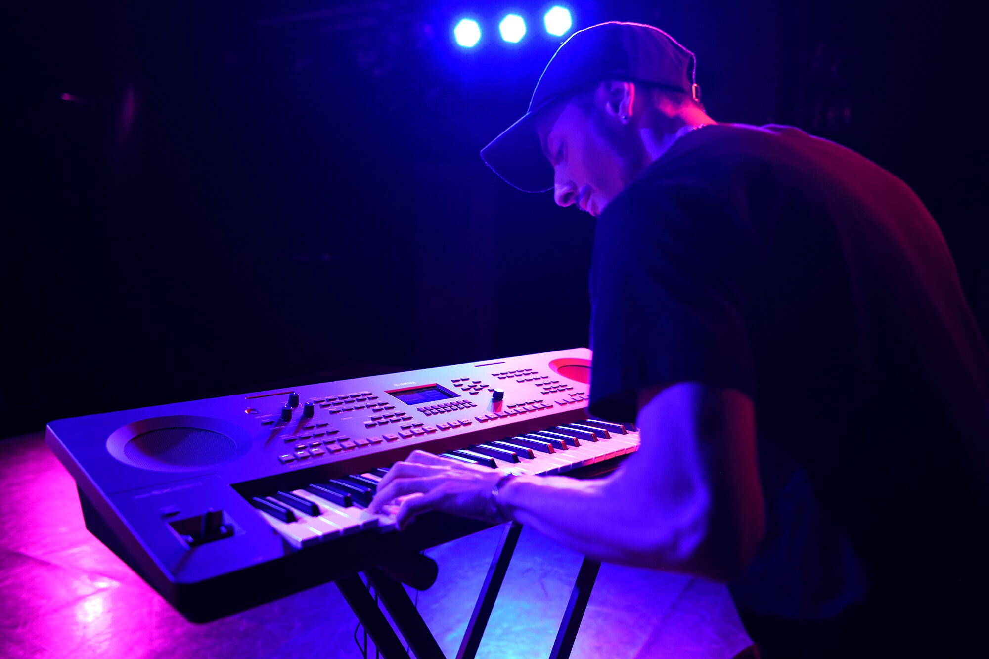 Una persona che suona una workstation arranger Yamaha su un supporto sotto le luci del palco