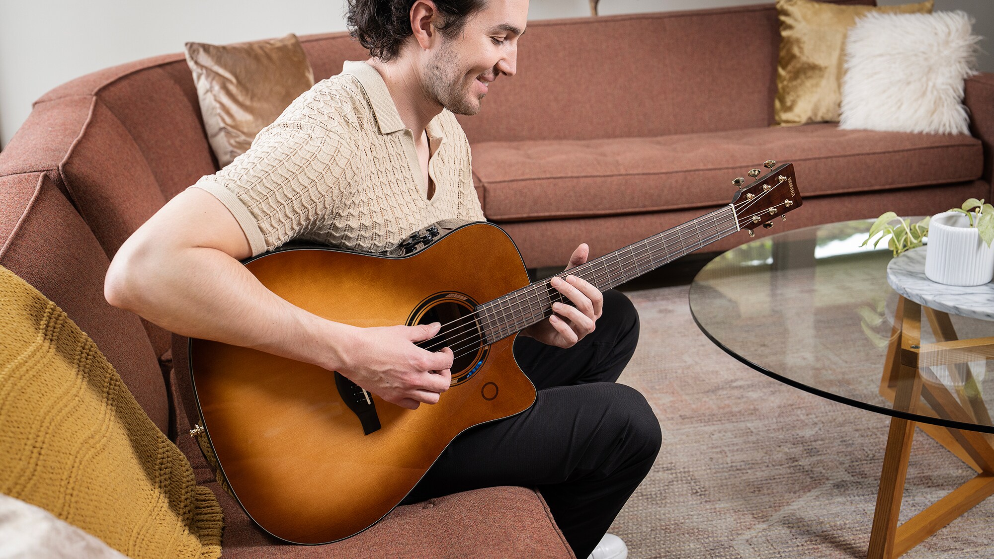 Un uomo seduto sul divano nel soggiorno che suona una chitarra acustica TAG3 C