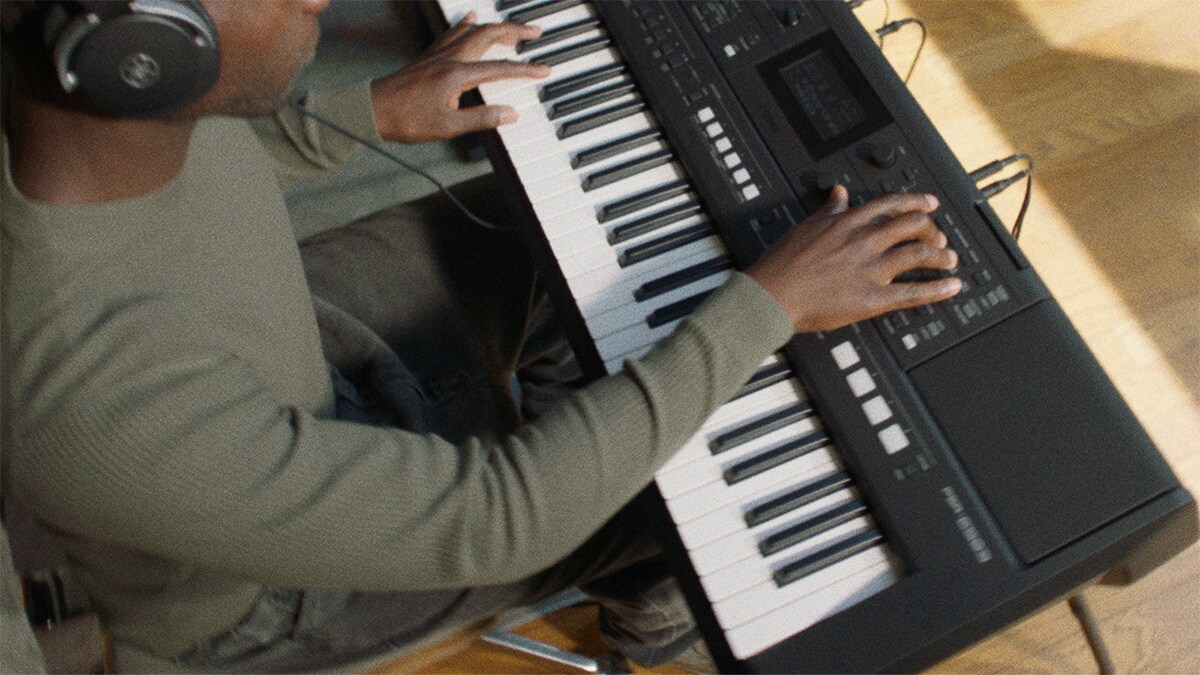 Una persona che suona la tastiera portatile Yamaha PSR-E483 con le cuffie