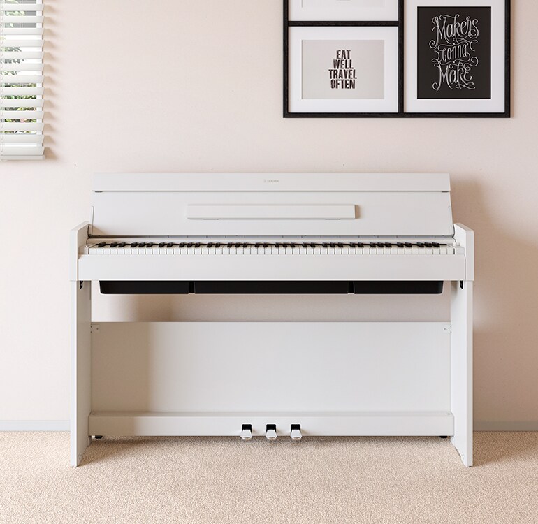 Un soggiorno con un pianoforte ARIUS bianco posizionato accanto a mensole a muro su cui si trovano lampade e un diffusore, armoniosamente integrato con l’arredamento.